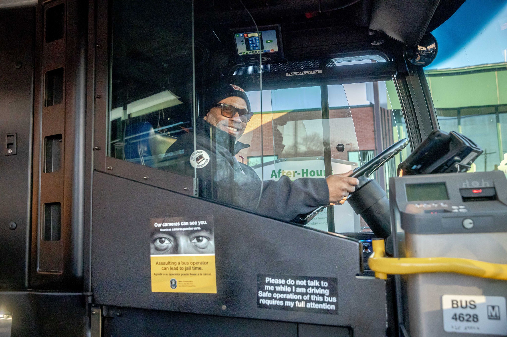 A bus driver sitting in the drivers seat behind plexiglass