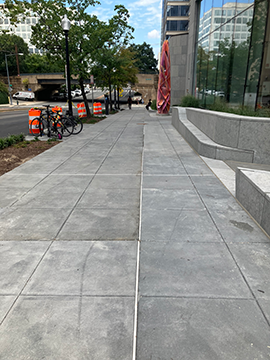 A picture of a sidewalk down 7th Street. The WMATA Headquarters building is on the left, and the street is on the right. There is landscaping and some construction cones to the right before the street.