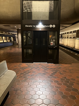A picture of the elevator from the lower level to the upper level. To the left there is a stone bench and on both sides there are train tracks for the Orange, Blue, and Silver line trains.