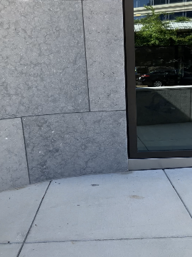A picture of the sidewalk in front of the Transit Accessibility Center building. There is a window pane to the right of the picture.