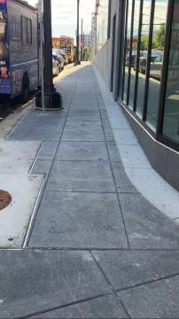 The picture shows the sidewalk down Virginia Avenue to the Transit Accessibility Center. The sidewalk is narrow with the street on the left and a building on the right.