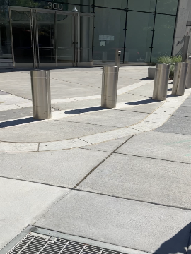 A picture of the entrance to the WMATA Headquarters building. There are bollards in the foreground of the picture and the entrance is in the background.